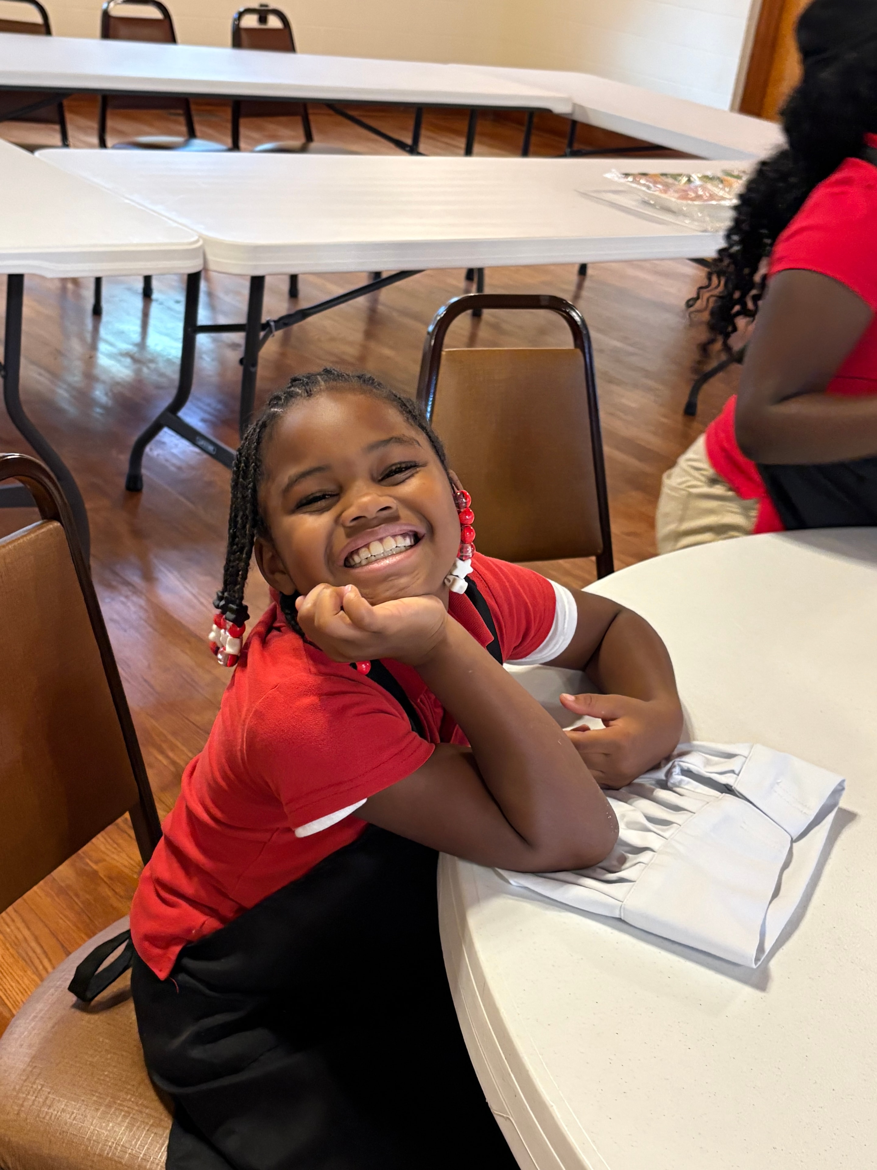 A smiling young chef in a red shirt enjoying a Kids R Cookin' session